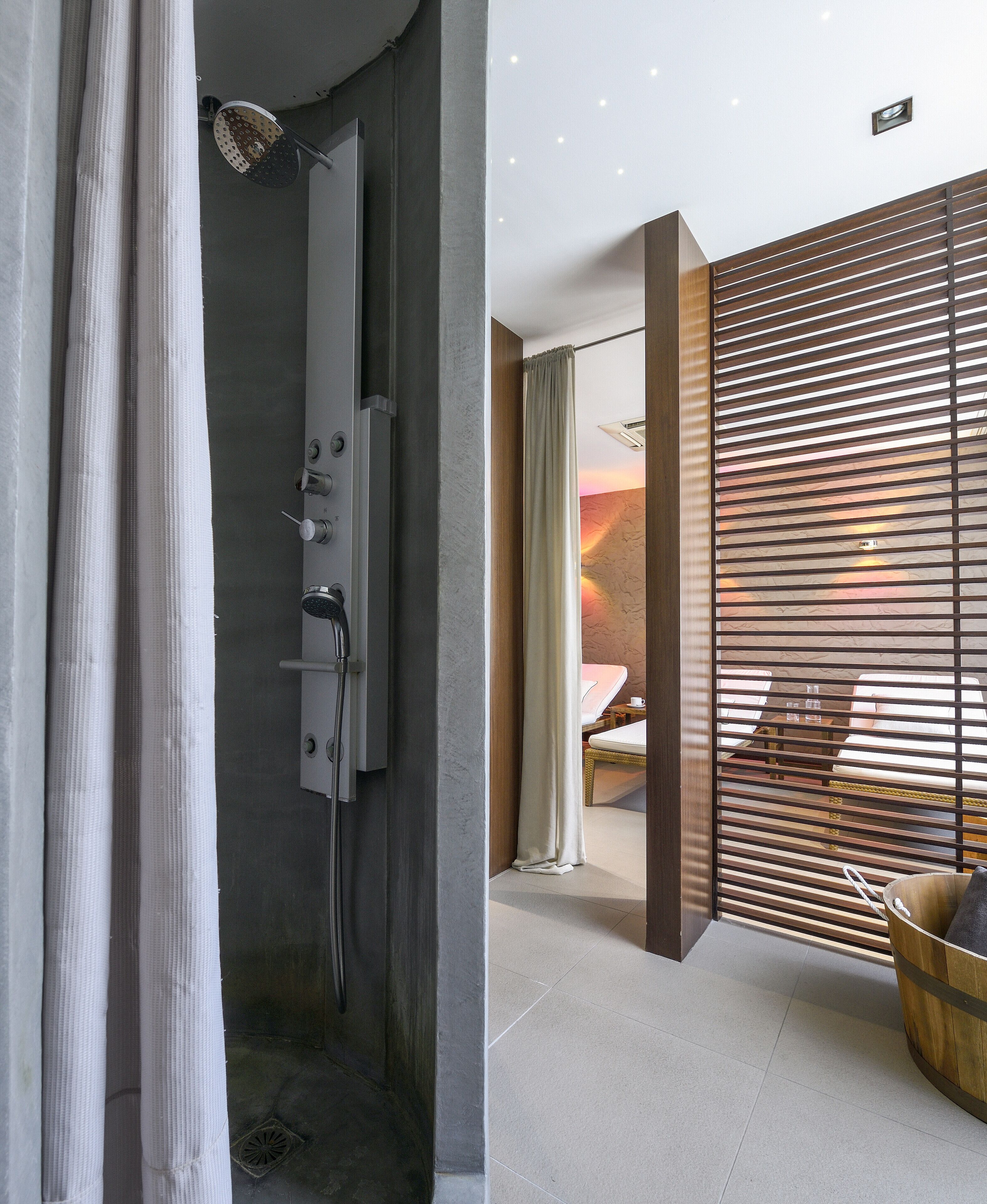A modern bathroom with a shower, a toilet, and a sink. There is a wooden partition with horizontal slats and a small window.