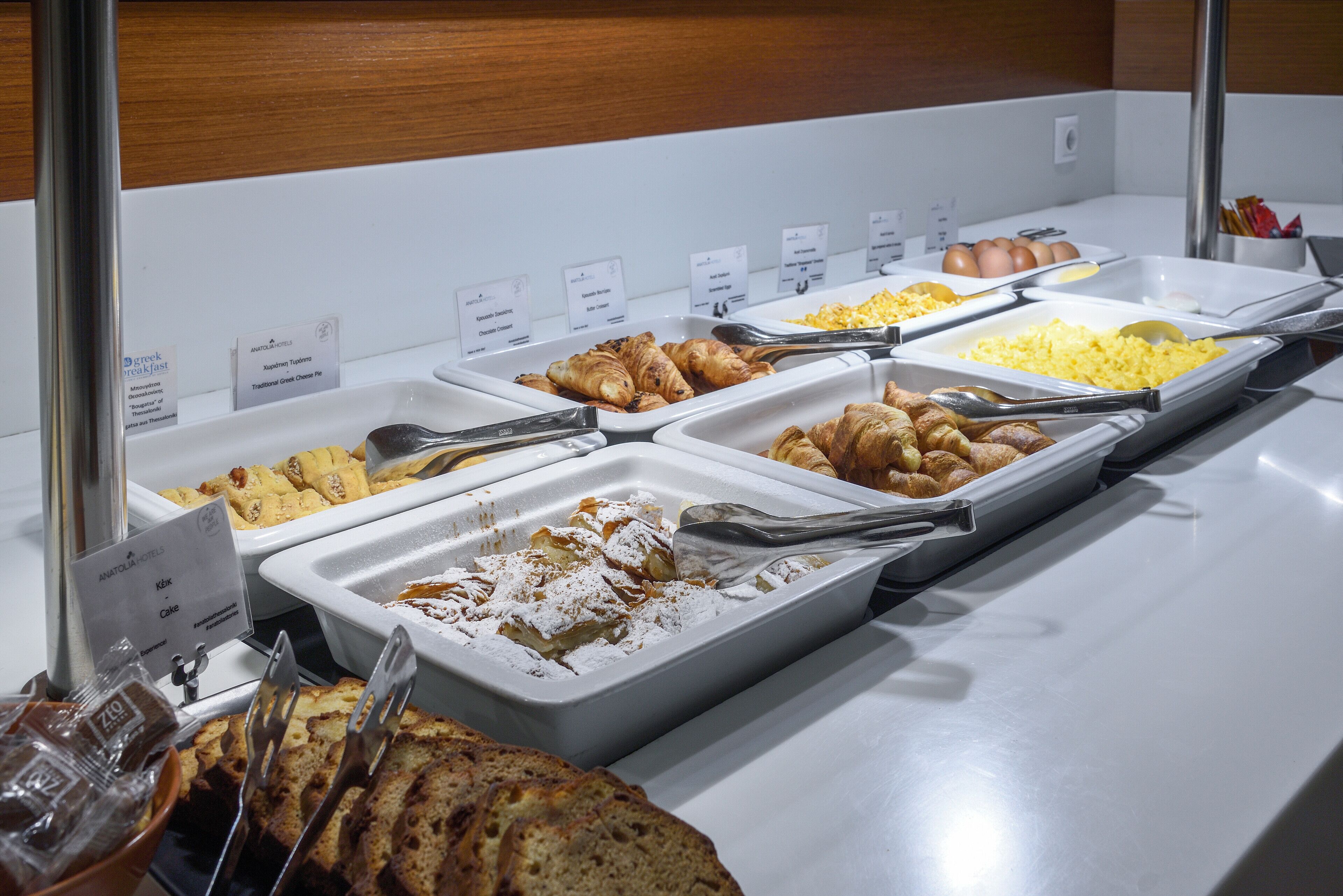 Un bufé con diversas opciones de comida, como pan, bollería y huevos.