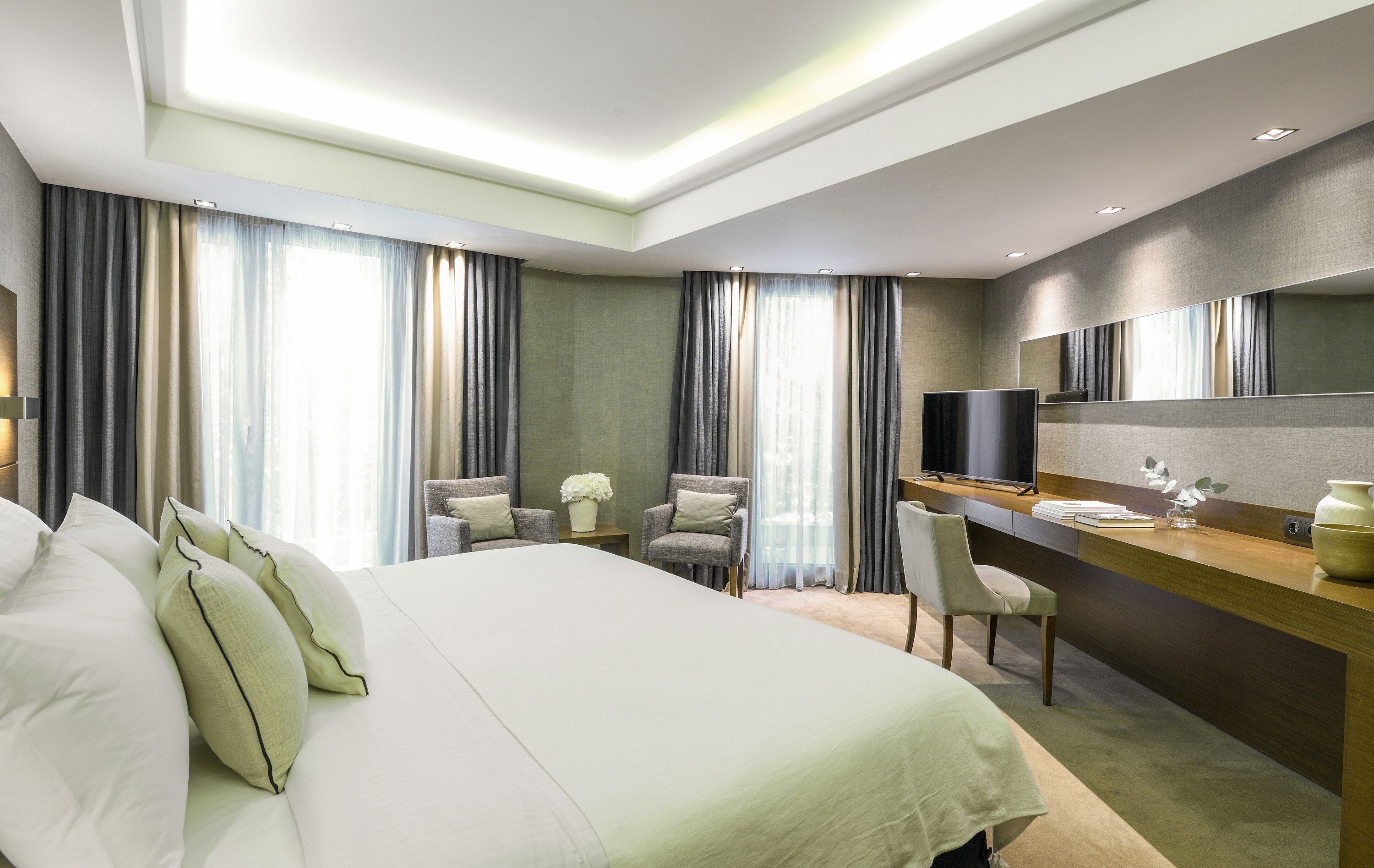 Une chambre d’hôtel moderne avec un grand lit, un bureau, une chaise et un grand miroir.