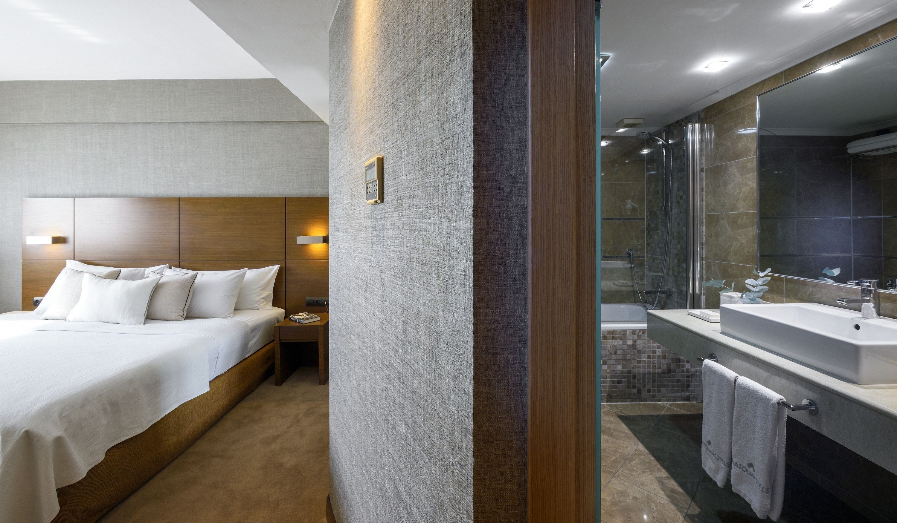 A hotel room with a large bed, a nightstand, a bathroom with a large mirror, a bathtub, and a sink.