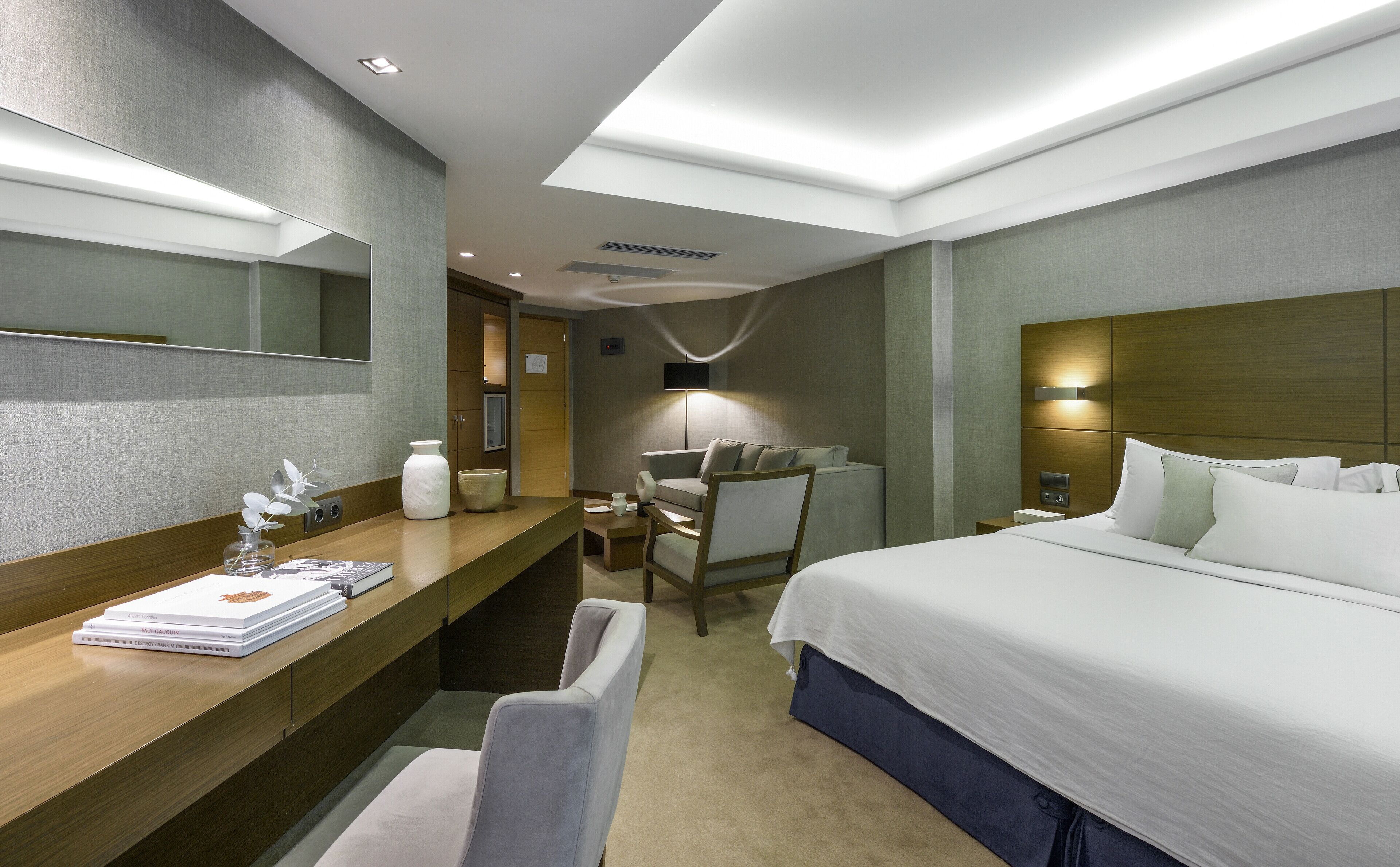 Una habitación de hotel con una cama, un escritorio con lámpara, una silla y un espejo grande.
