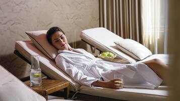 A person lying on a sun lounger in a room with a patterned wall and a window with curtains.