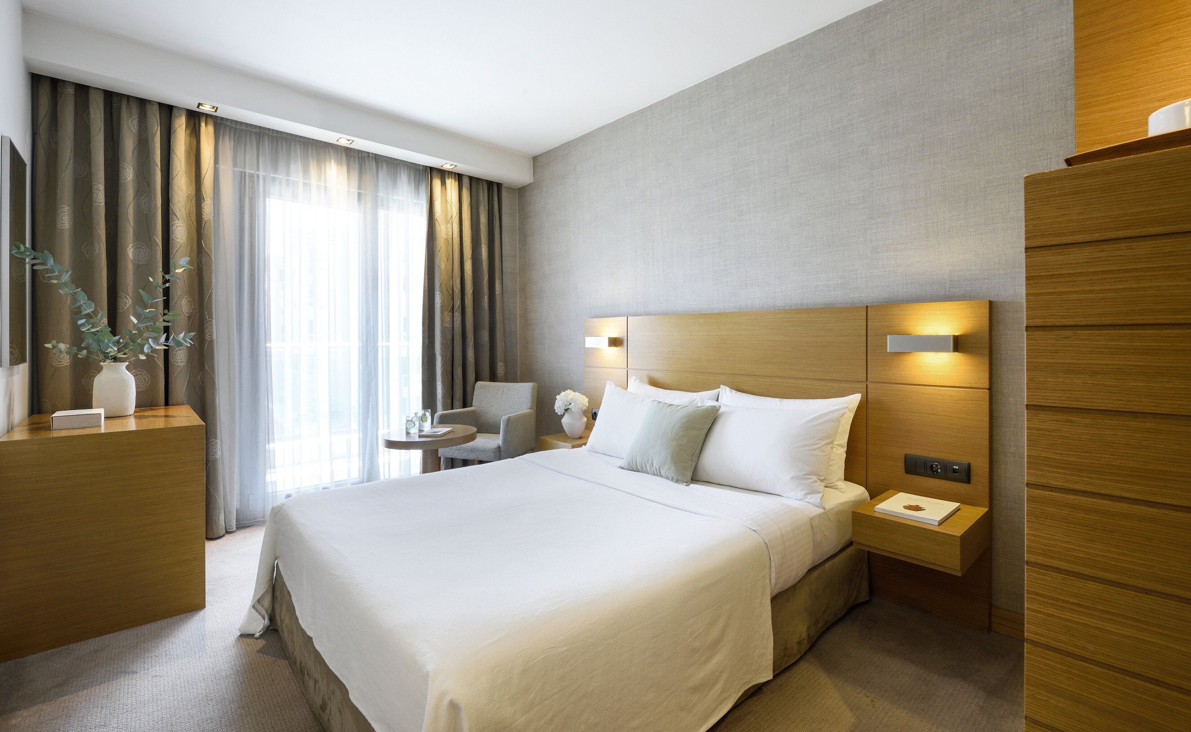 A hotel room with a large bed, bedside tables, a chair, and a desk with a vase of flowers.