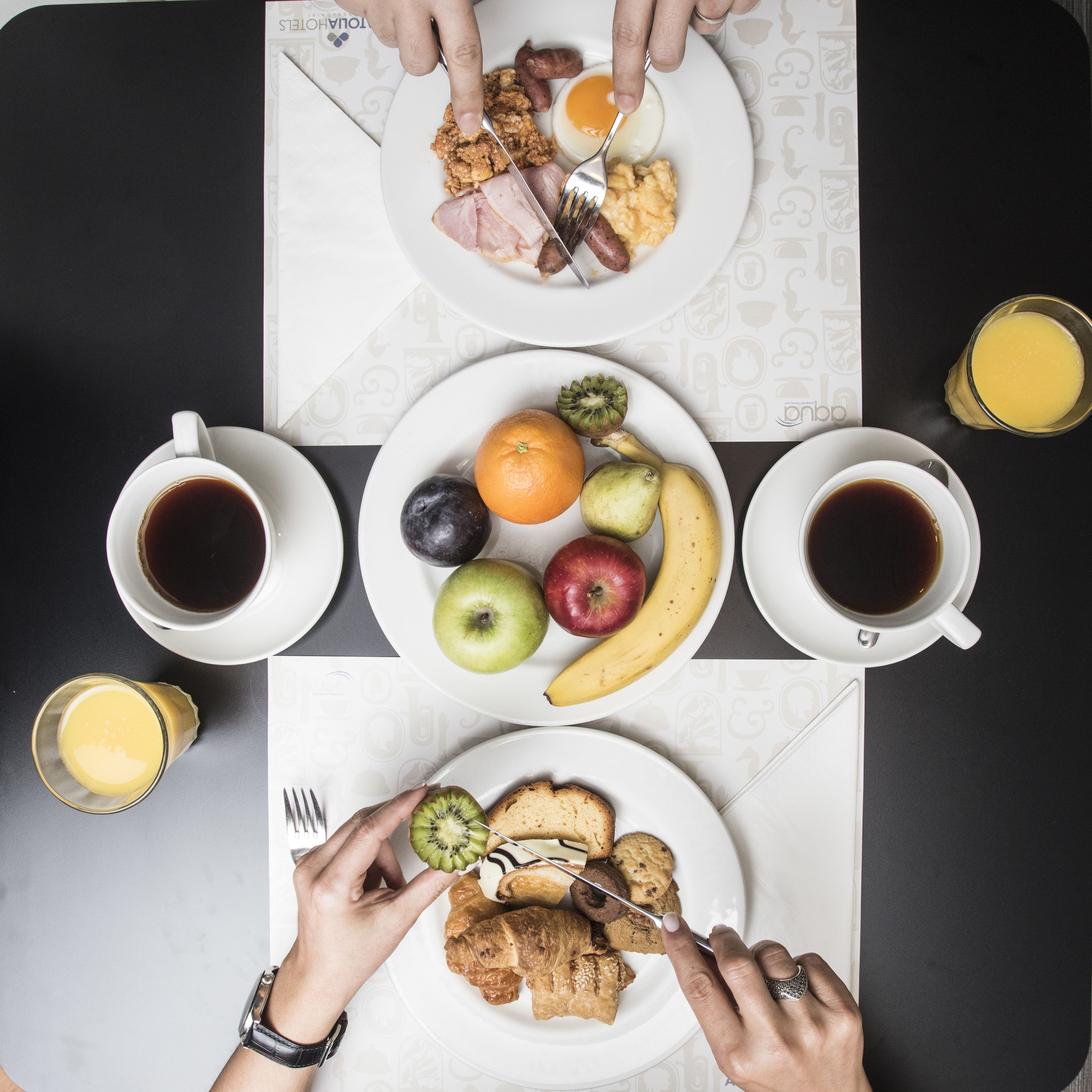 Une table mise pour le petit-déjeuner, avec des assiettes de nourriture, des tasses de café et un verre de jus d’orange.