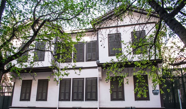 A two-story building with multiple windows and a tree in front. - Anatolia (Thessaloniki)
