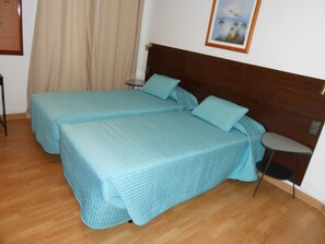 A room with two beds, wooden flooring, a nightstand, and a painting on the wall.
