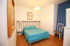 Un dormitorio con una cama, una silla, una mesita de noche, una lámpara y un cuadro en la pared.