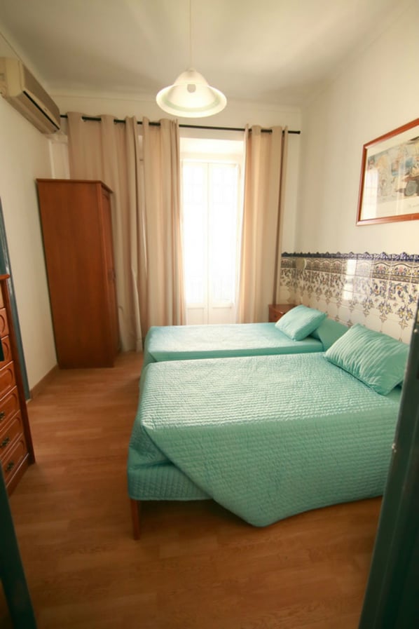 Un dormitorio con dos camas, un armario de madera, un ventilador de techo y una ventana con cortinas.