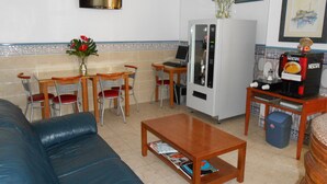 Ein Wohnzimmer mit einem blauen Sofa, einem Holztisch und einem Essbereich mit einem weißen Kühlschrank und einer Nescafé-Kaffeemaschine.