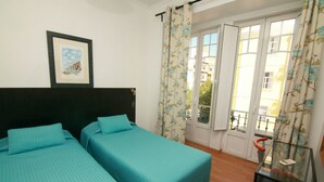 Ein Zimmer mit zwei Betten, einem gerahmten Bild an der Wand, einem Glastisch und einer Tür zu einem Außenbereich.