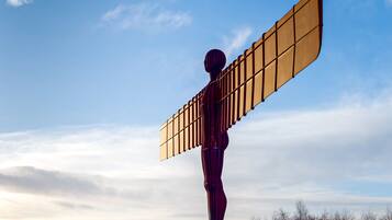 A large metallic sculpture of a figure with outstretched arms, set against a clear sky.