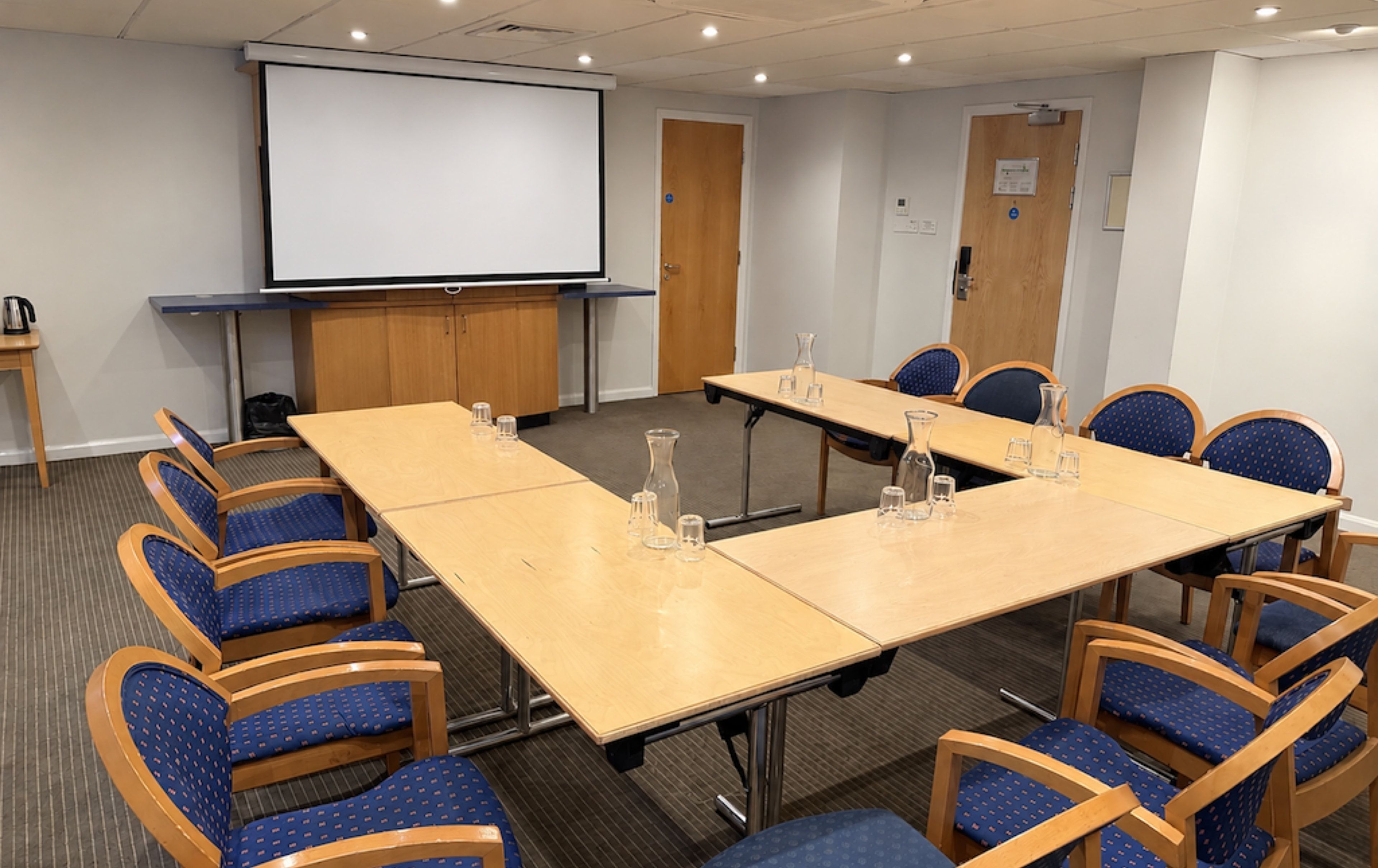 A conference room with a large table, chairs, a projector screen, and a door.