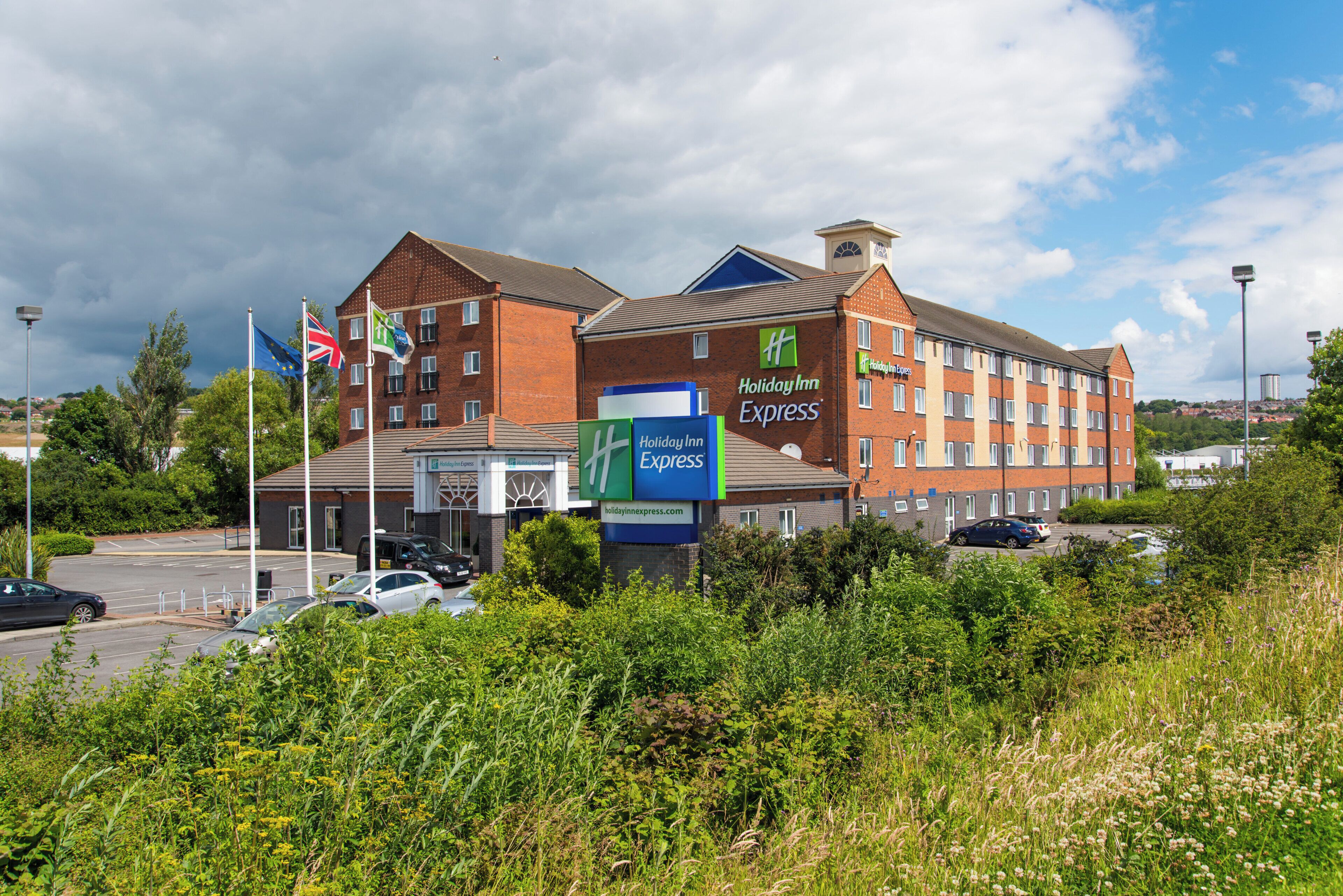Un hotel Holiday Inn Express de varios pisos, con estacionamiento y banderas.