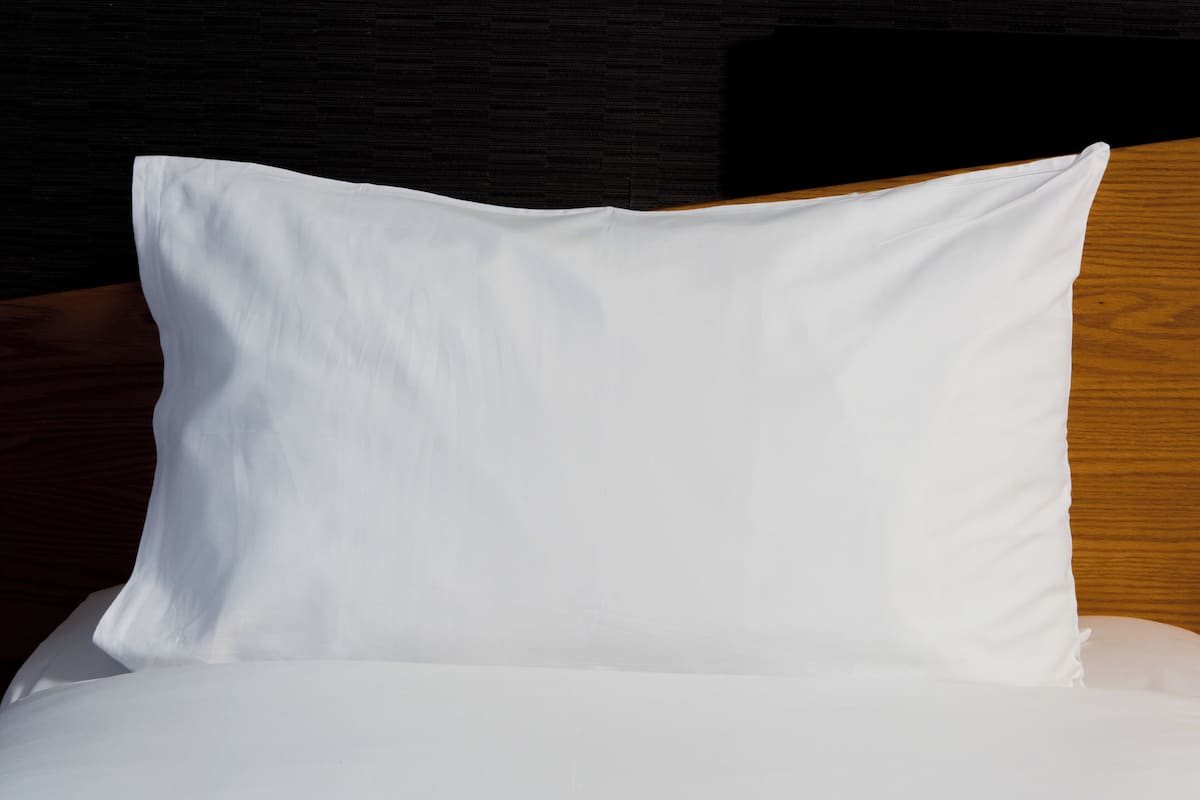 A white pillow on a bed with a wooden headboard.