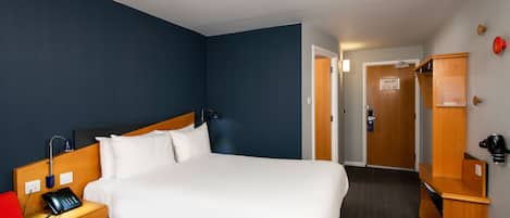 A hotel room with a single bed, bedside table, and a desk with a telephone.