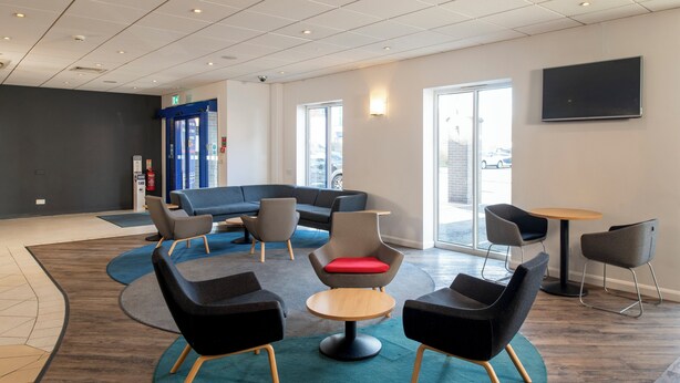 A modern lounge area with a sectional sofa, round tables, and comfortable chairs. - Holiday Inn Express Newcastle Gateshead by IHG (Newcastle-upon-Tyne)