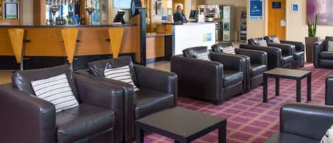 Un vestíbulo de hotel con sofás de cuero, un mostrador de recepción y una zona de bar.