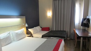 Habitación de hotel con dos camas, un escritorio, una silla, un televisor y una ventana con cortinas.