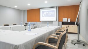 Un salón de conferencias con una larga mesa, sillas, una pantalla de proyector y una presentación sobre Holiday Inn Express.