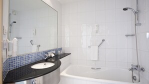 Un baño moderno con lavamanos blanco, encimera negra y una bañera grande.
