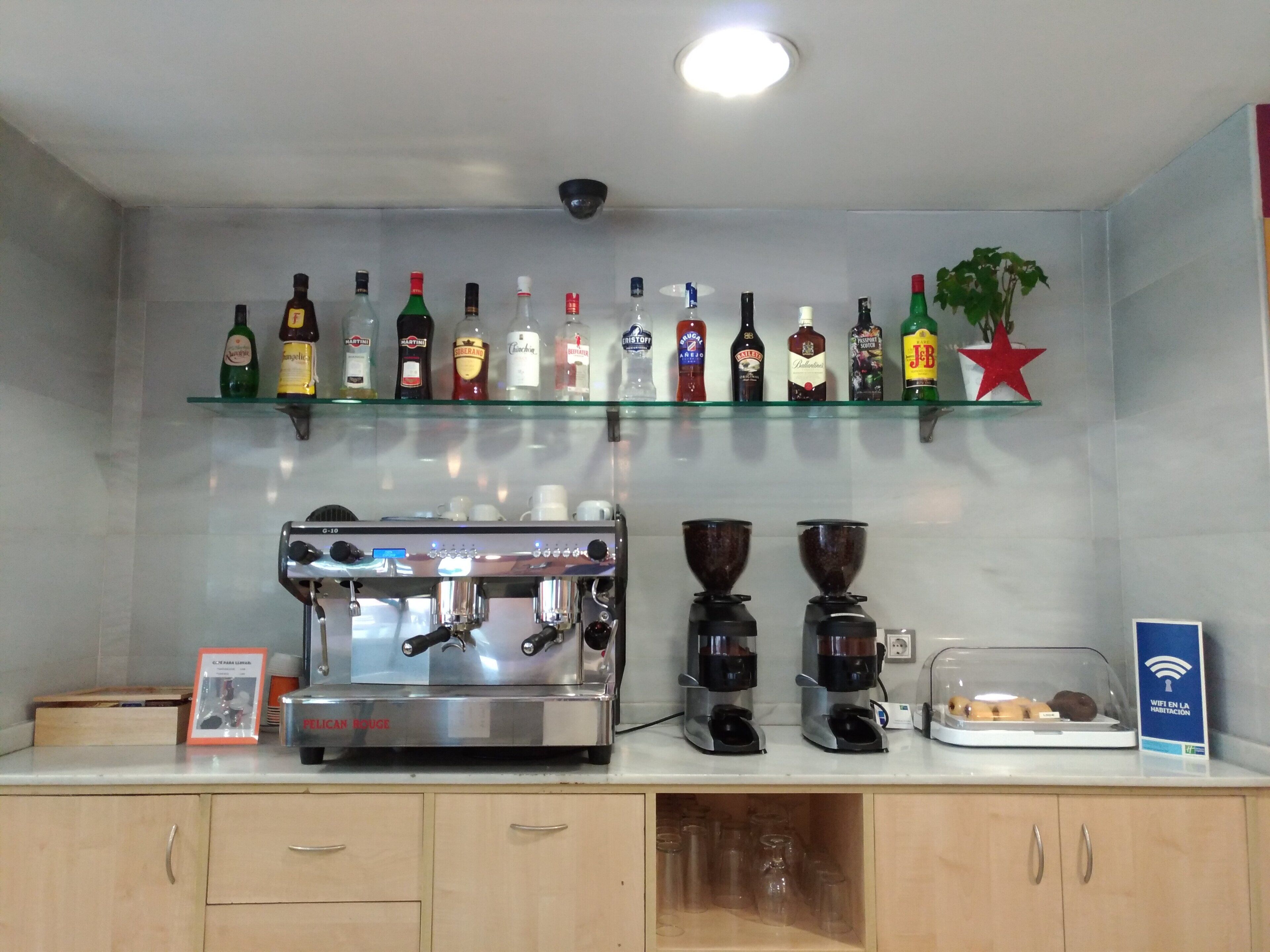 Zona de bar con una máquina de café, estantes llenos de botellas de licor y un cartel de WiFi.