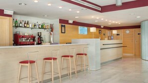 Un vestíbulo de hotel con zona de bar, taburetes, una máquina de café y un cartel que indica las tarifas de las habitaciones.
