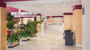 Vestíbulo de hotel con mostrador de recepción, zona de estar y plantas en macetas.