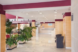 Vestíbulo de hotel con mostrador de recepción, zona de estar y plantas en macetas.