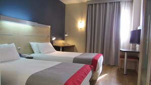 Habitación de hotel con dos camas, un escritorio, una silla, un televisor y una ventana con cortinas.