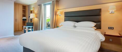 A hotel room with a large bed, a desk, a chair, and a wardrobe.