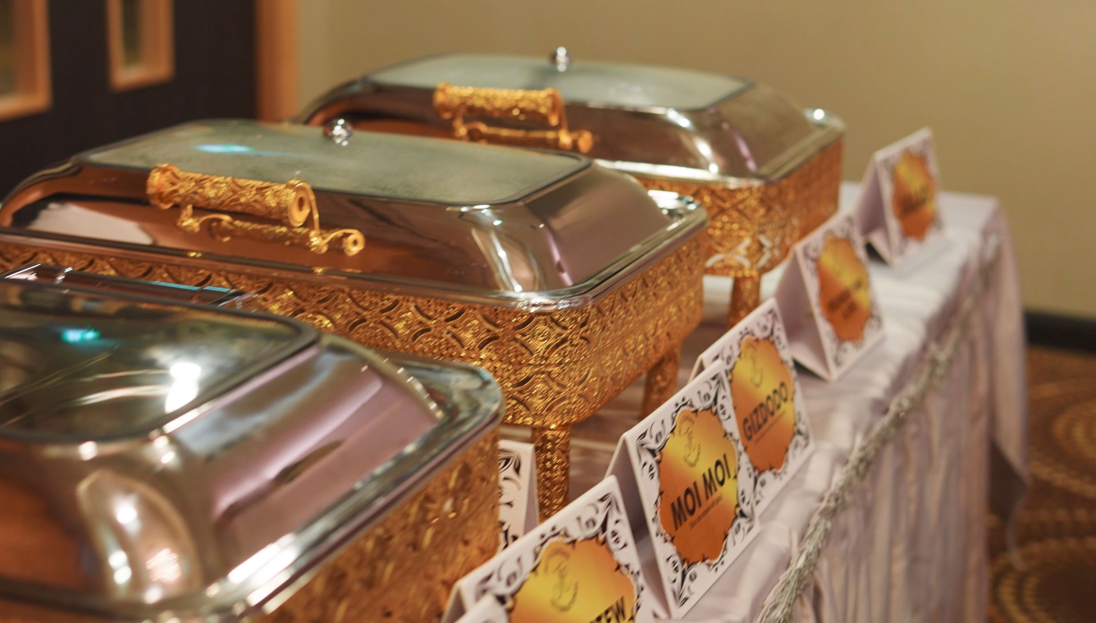 A buffet table with covered food containers and a sign indicating 'MOI MOI'.