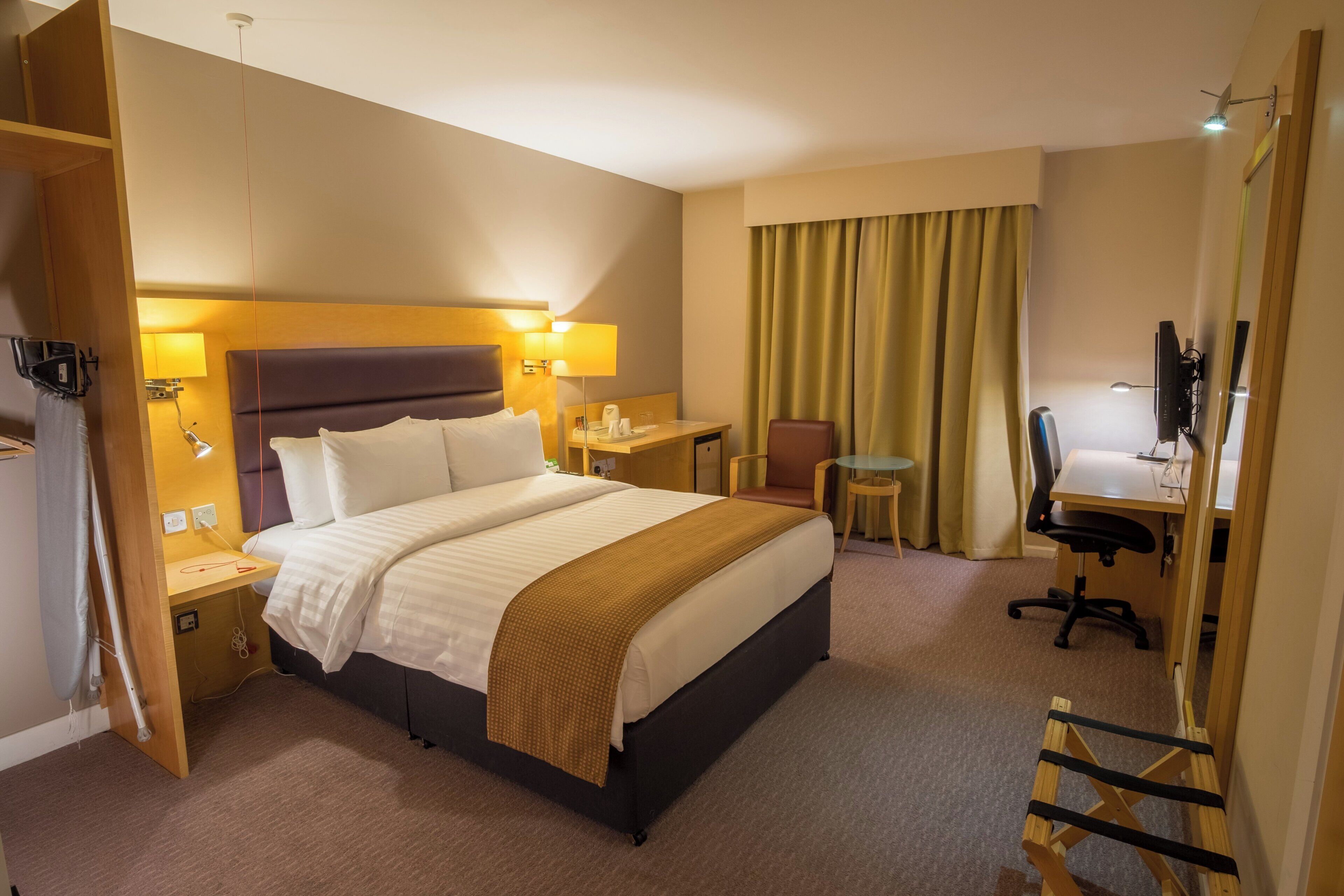 A hotel room with a bed, bedside tables, a desk, a chair, a television, and a wardrobe.