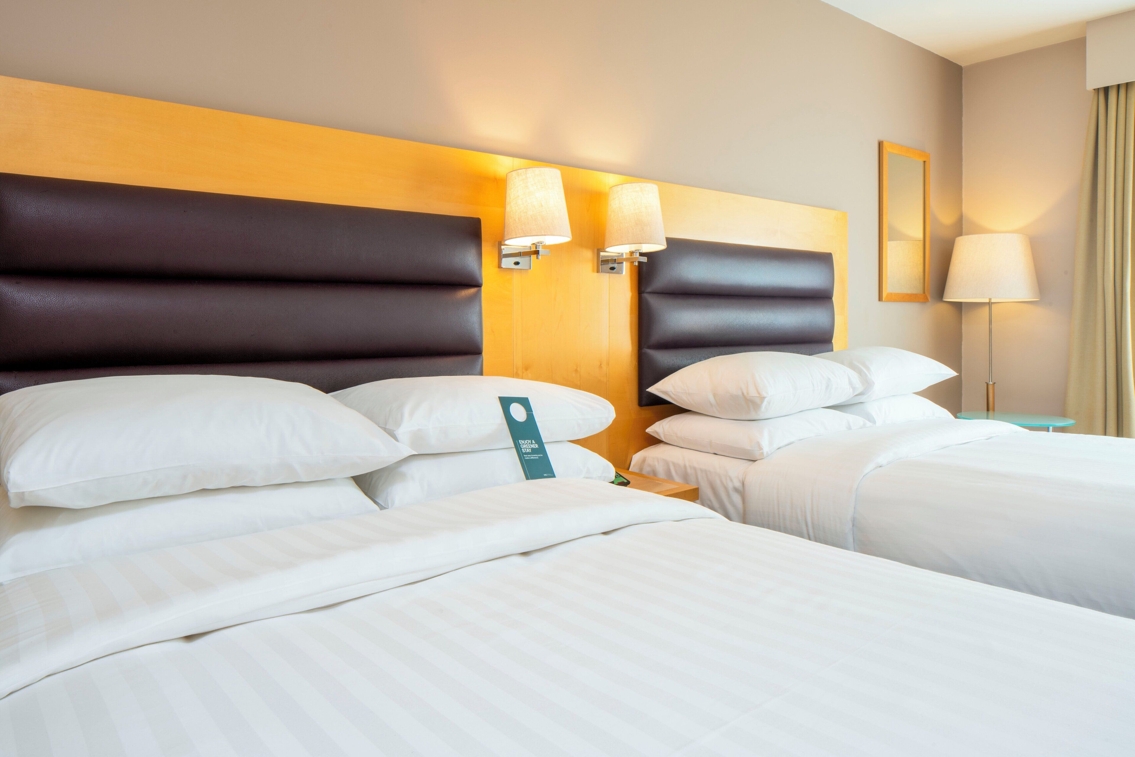A hotel room with a large bed, two bedside tables, a headboard, and a mirror on the wall.