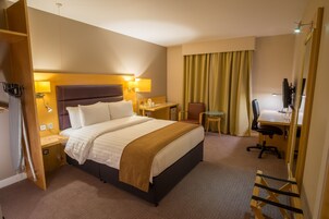 Una habitación de hotel con una cama grande, mesitas de noche, un escritorio, una silla y un espejo.