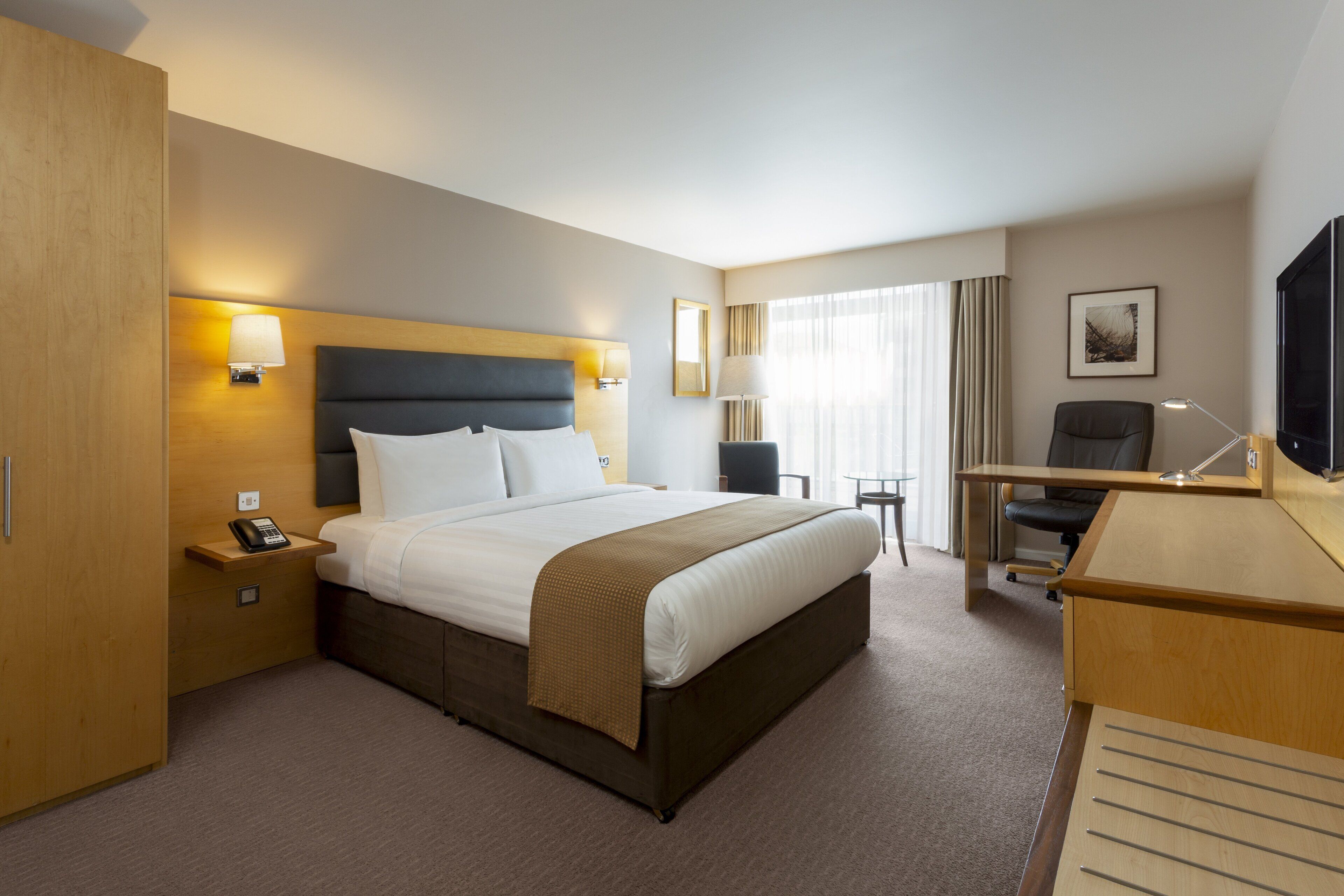 Habitación de hotel con cama, mesita de noche, lámpara, escritorio, silla y televisión.