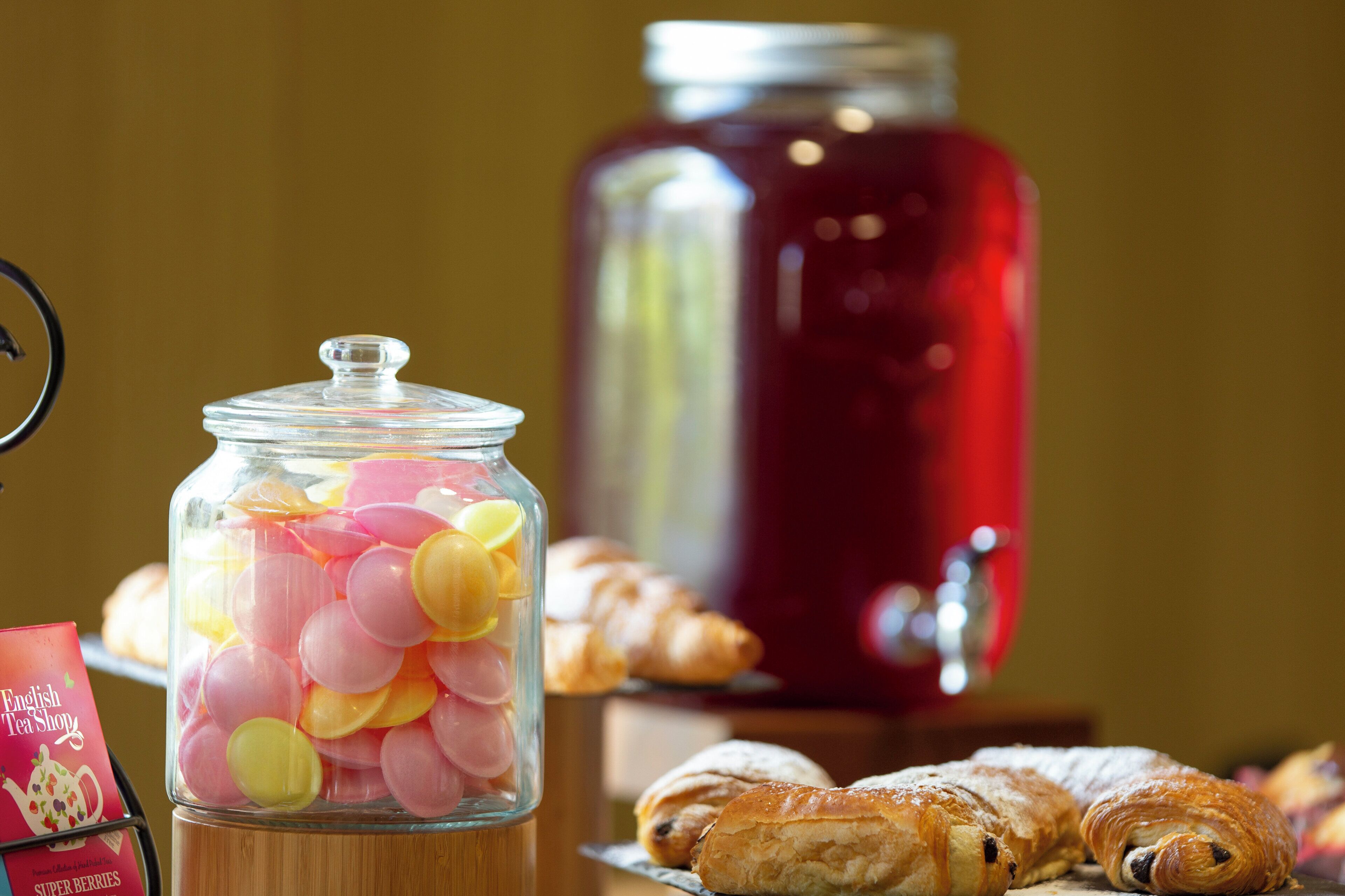Un frasco de vidrio lleno de caramelos de colores, un recipiente rojo para bebidas y pasteles sobre una mesa.