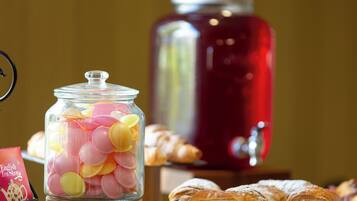 Un frasco de vidrio lleno de caramelos de colores, un recipiente rojo para bebidas y pasteles sobre una mesa.