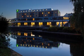 Ein Hotel mit mehreren Etagen, einem spiegelnden Wasserspiegel davor und einer gut beleuchteten Fassade.