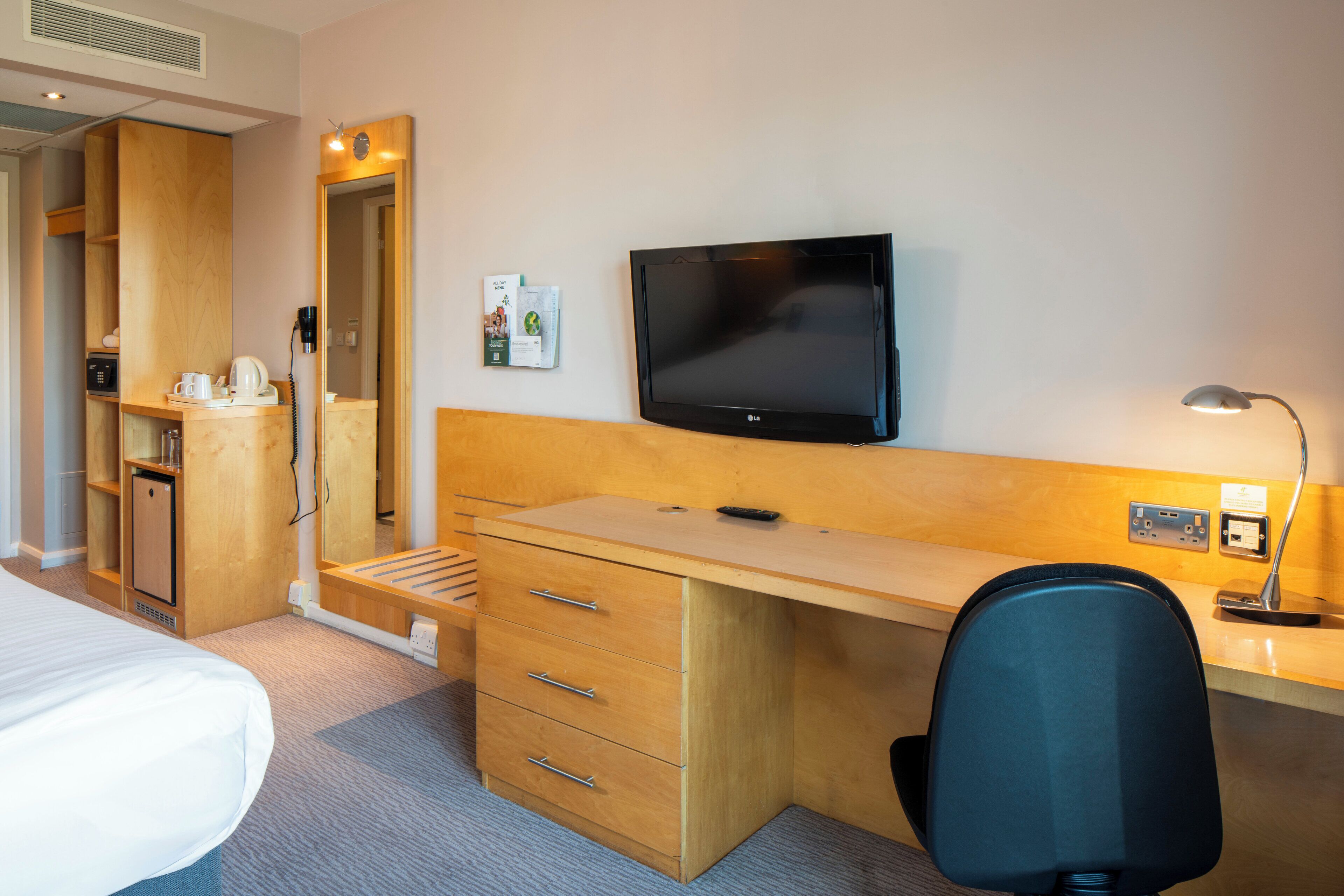 A hotel room with a bed, wooden desk, chair, television, and a small kitchenette.