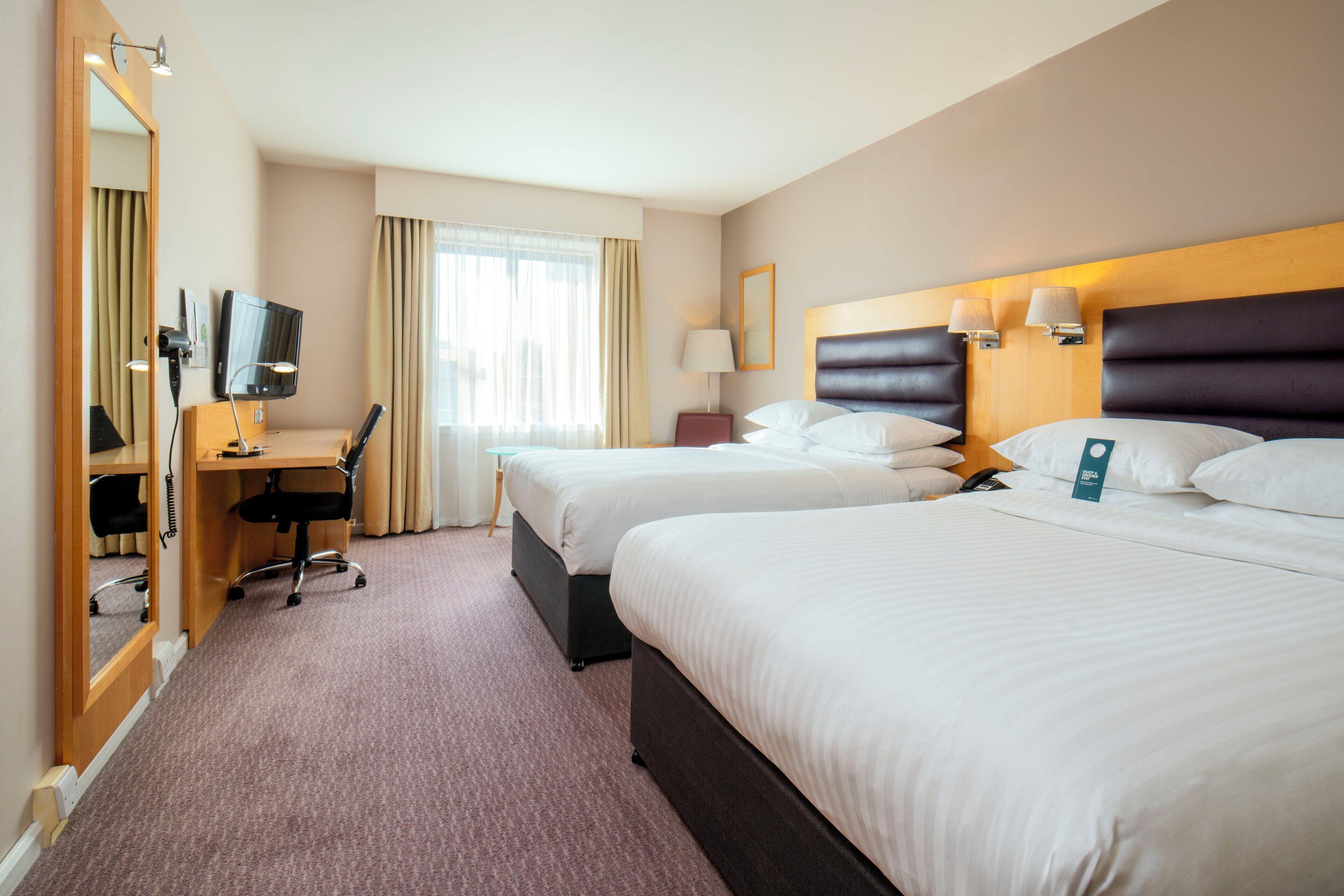 Une chambre d’hôtel avec deux lits, un bureau, une chaise, une télévision et un grand miroir.