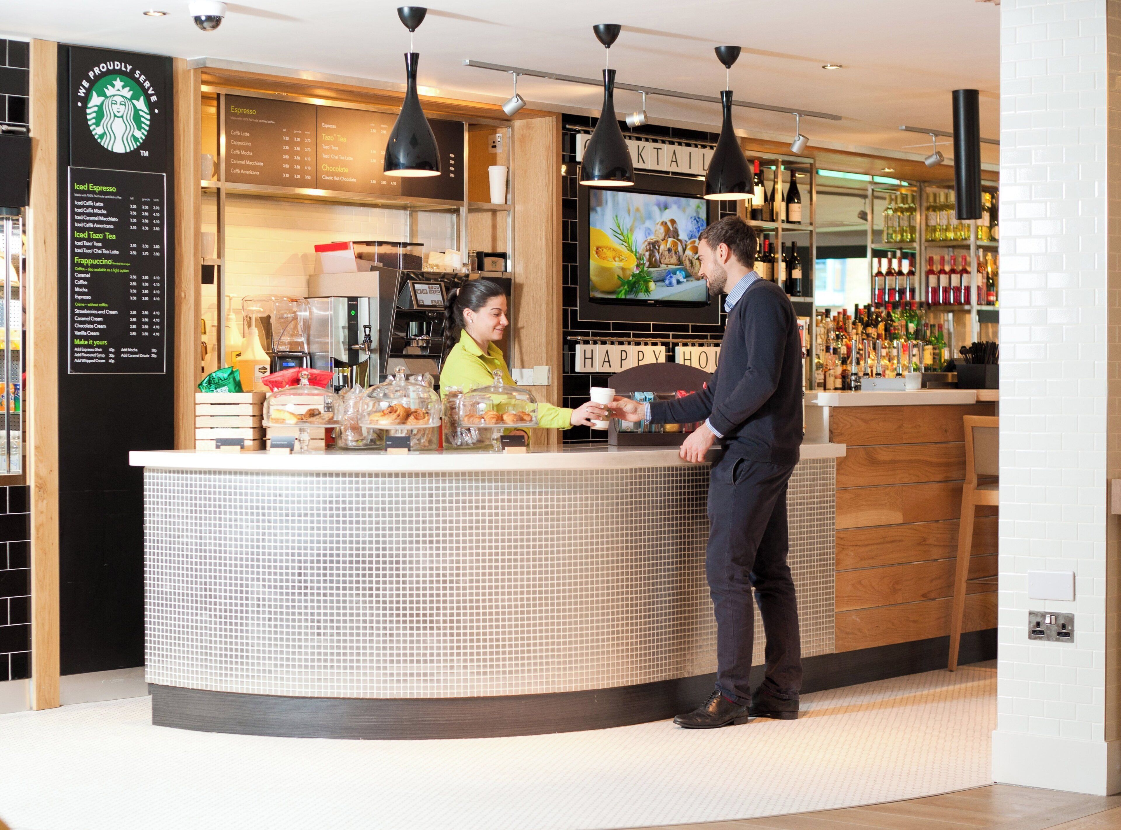 A Starbucks counter with a menu, a beverage dispenser, and a display of pastries.