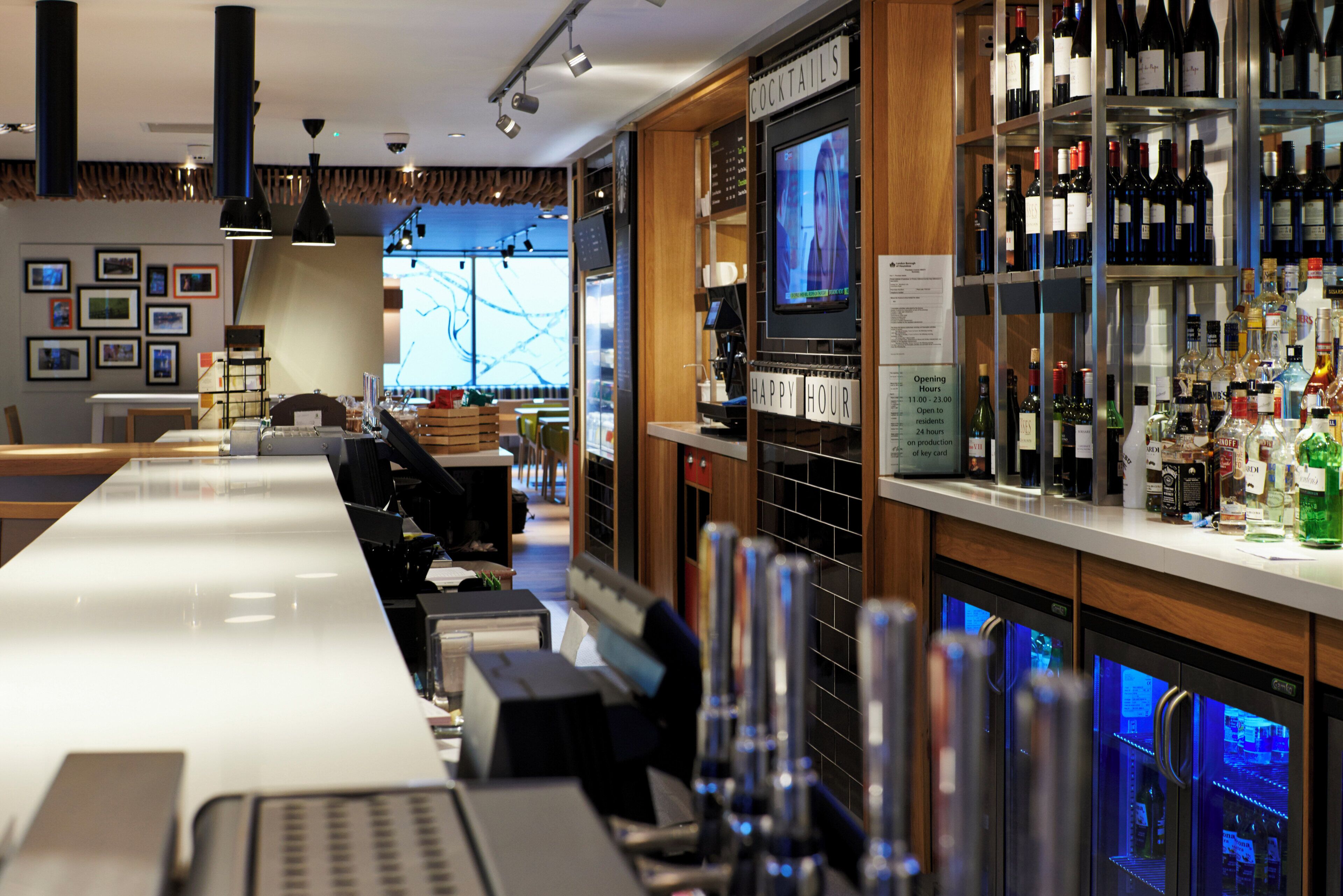 En bar med en lang disk, hylder med flasker og et fjernsyn, der viser et program.