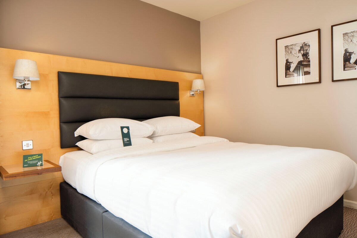 A neatly made bed with a black headboard, two bedside lamps, and framed pictures on the wall.