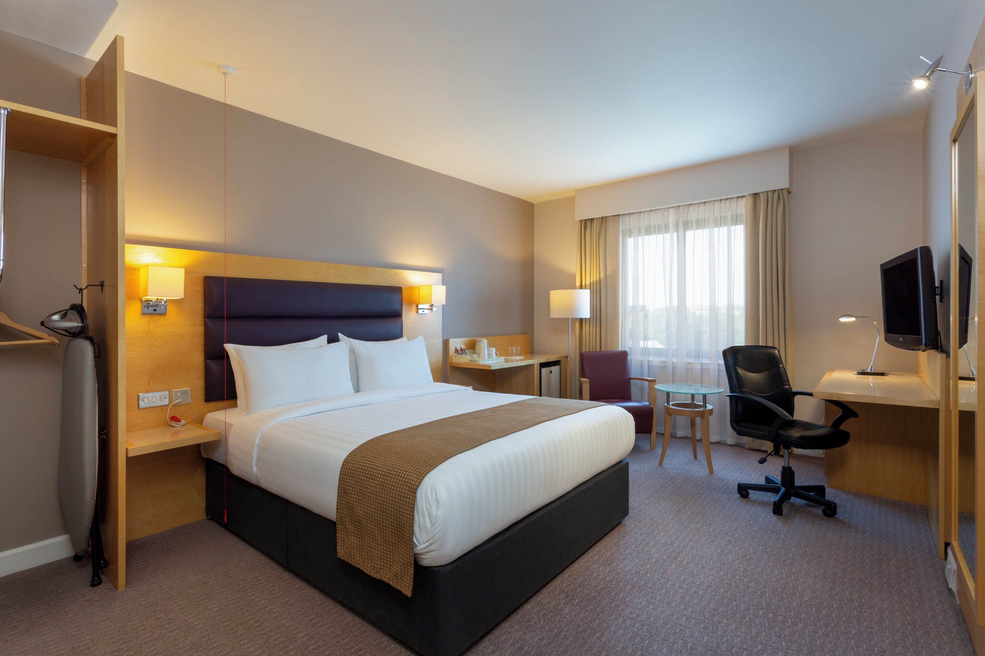 Een hotelkamer met een groot bed, nachtkastjes, een bureau, een stoel, een televisie en een raam met gordijnen.