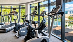 A gym with stationary bikes, treadmills, and a view of a body of water through large windows.