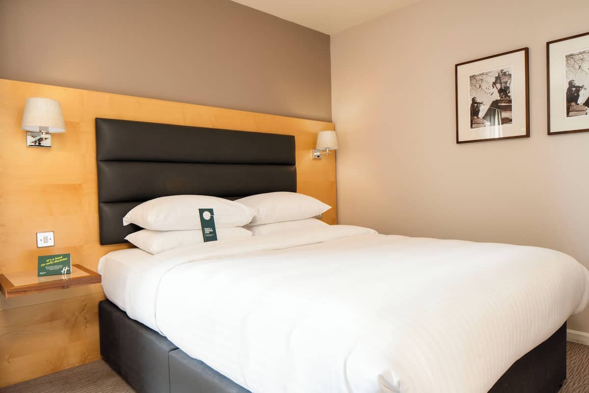 A neatly made bed with a black headboard, two bedside lamps, and framed pictures on the wall.