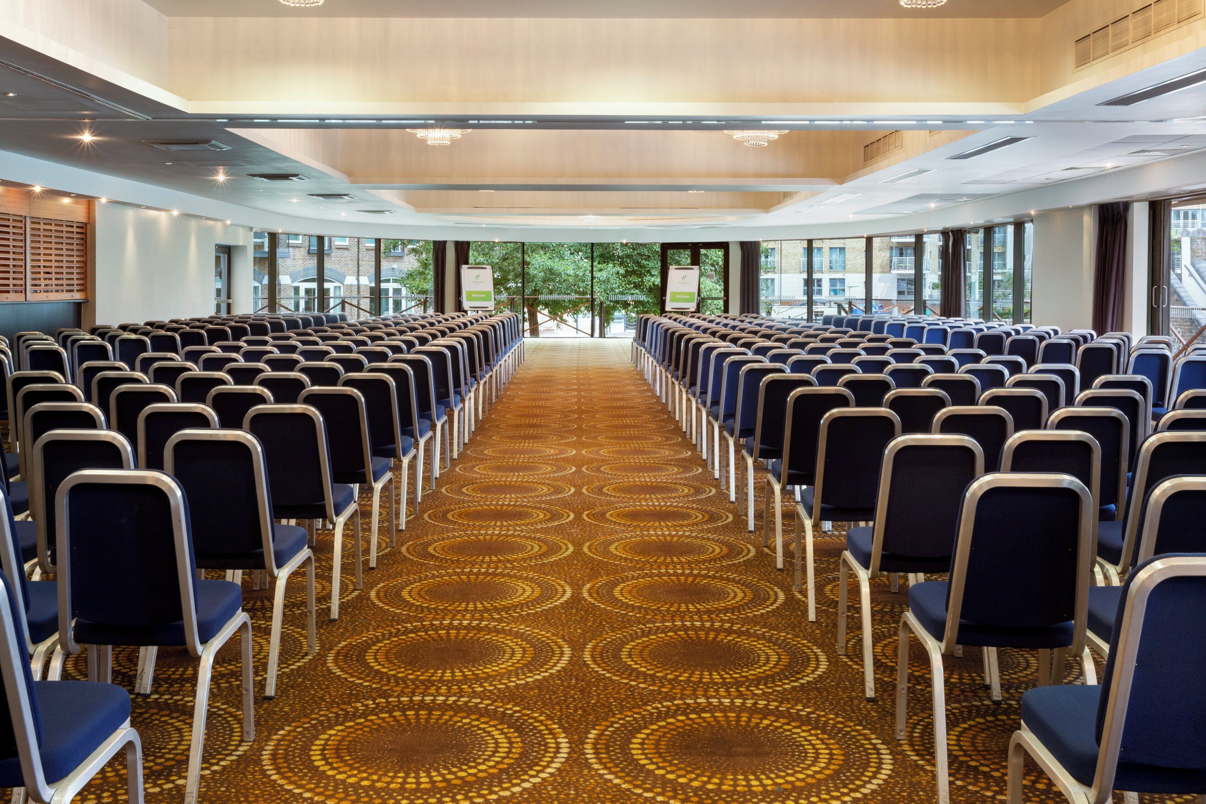 A conference room with rows of chairs, a patterned carpet, and large windows.