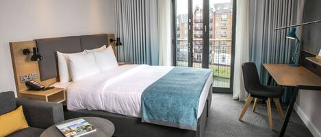 Habitación de hotel moderna con una cama grande, un escritorio, una silla y vistas a edificios por la ventana.