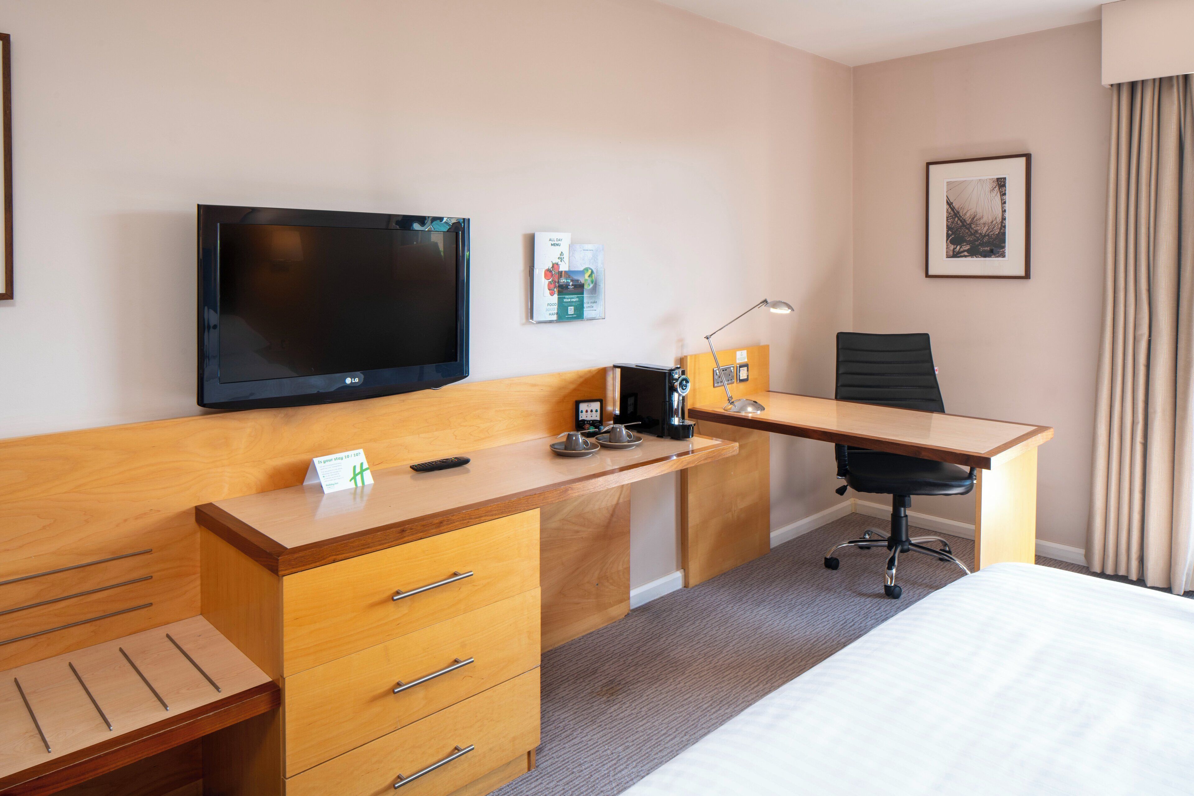 Ein Hotelzimmer mit Bett, Holztisch, Stuhl, Fernseher und einem kleinen Tisch mit Fernbedienung.