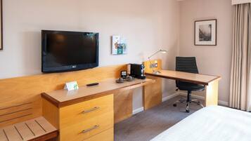 Quarto de hotel com cama, escrivaninha de madeira, cadeira, televisão e uma pequena mesa com controle remoto.
